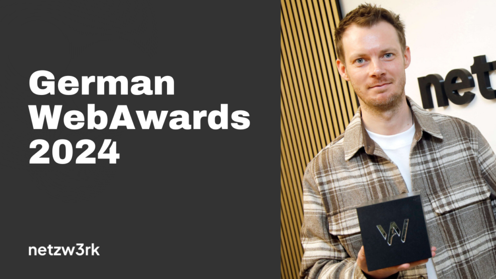Award recipient holding a black box with a W logo at the German WebAwards 2024 event. The man wears a plaid jacket, standing beside a backdrop.
